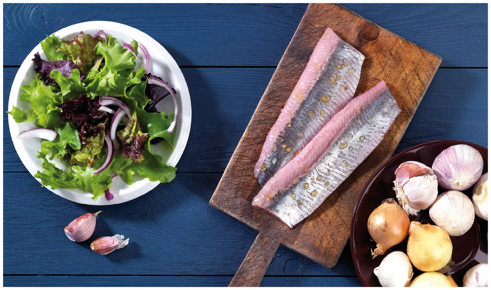 Matjesfilets auf Holzbrett neben Salat und Zwiebeln