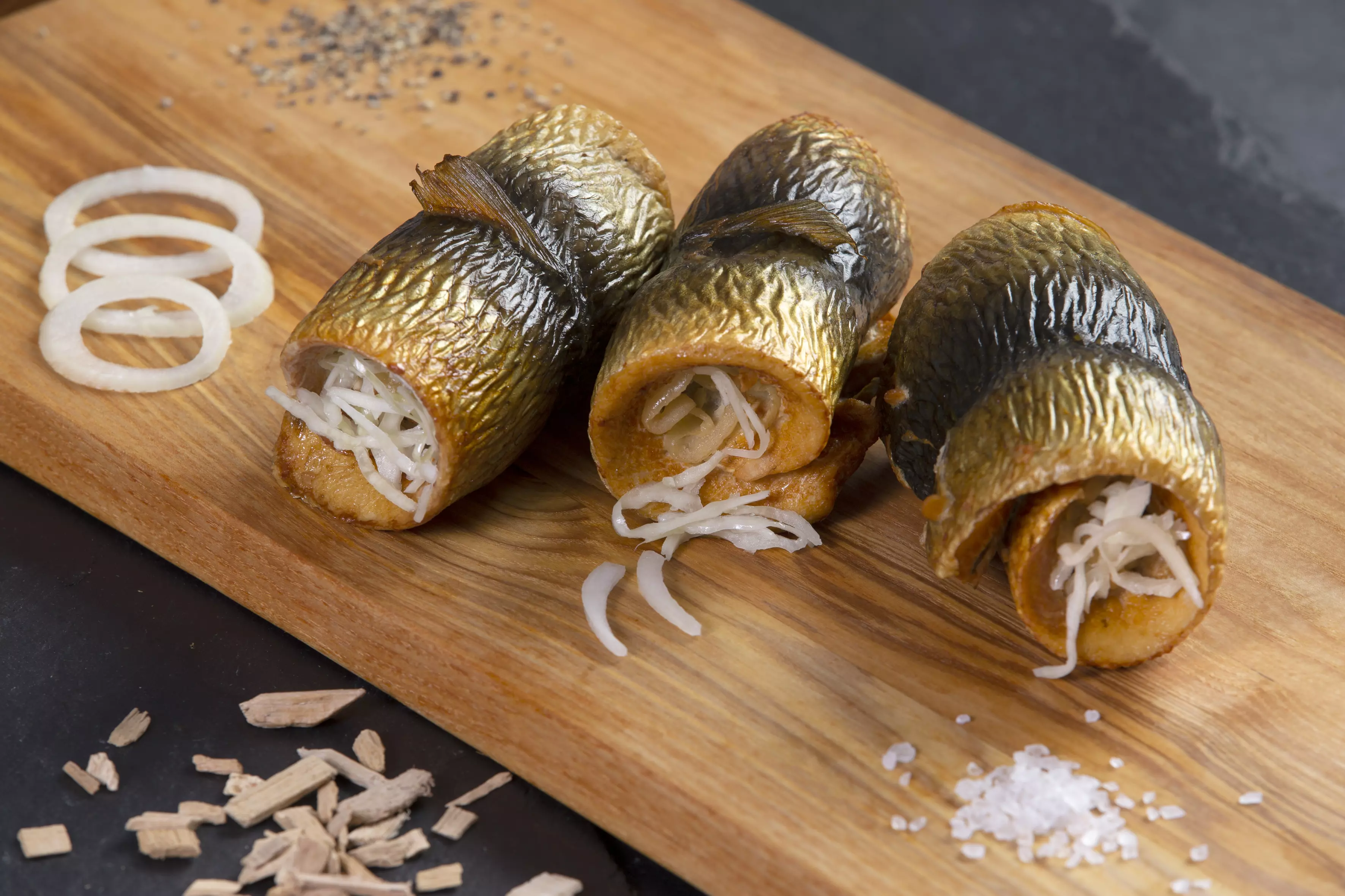 drei gerollte Bismarckheringe mit Zwiebeln auf Holzbrett