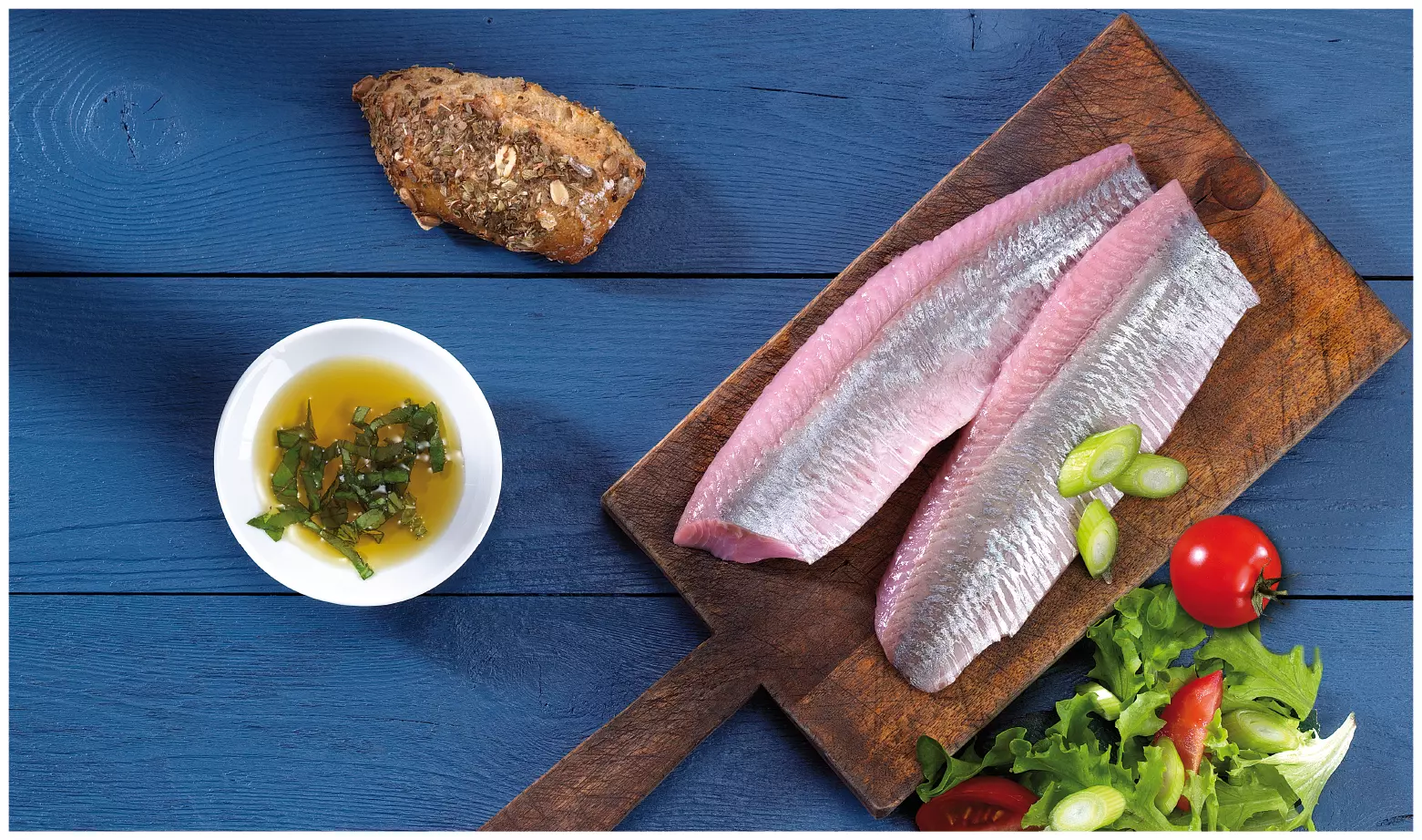 Zwei rohe Matjesfilets auf Holzbrett, daneben Brot, Öl und S