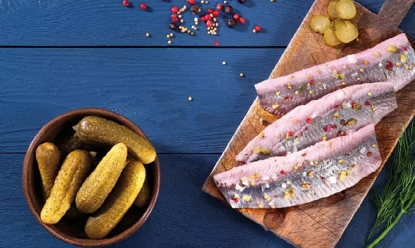 Heringsfilet mit Gewürzen auf Holzbrett, daneben Gewürzgurke