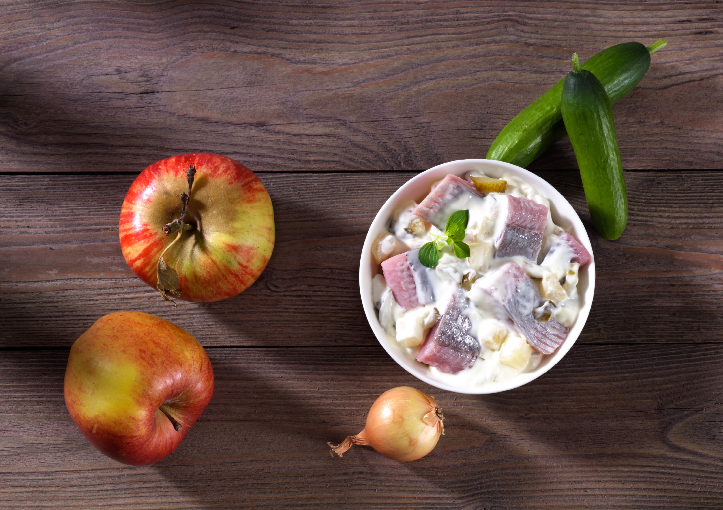 Schüssel mit Heringssalat, Äpfeln, Gurken und Zwiebel