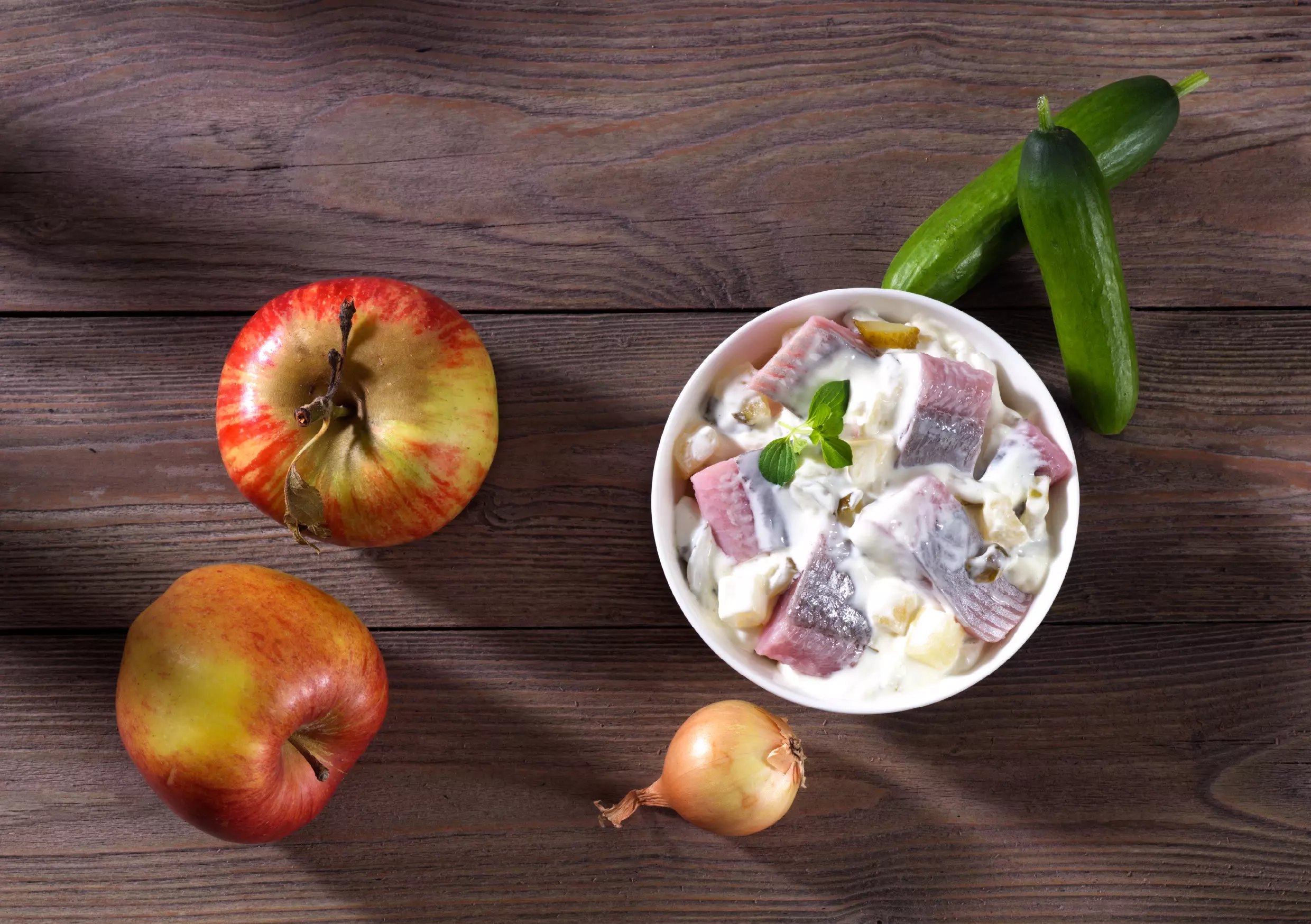 Schüssel mit Heringssalat, Äpfeln, Gurken und Zwiebel