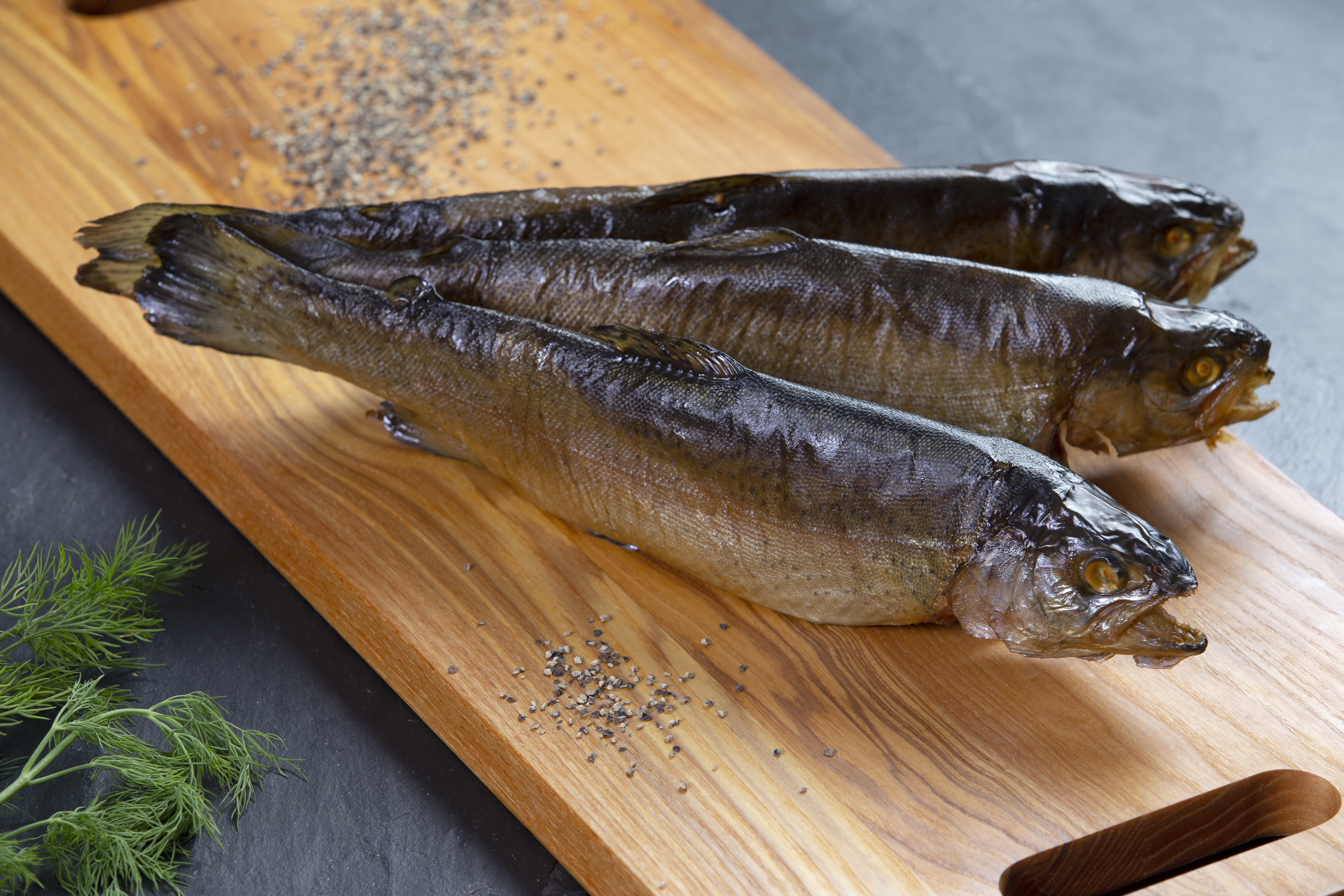 Geräucherte Fische auf einem Holzbrett mit Pfefferkörnern und Dill