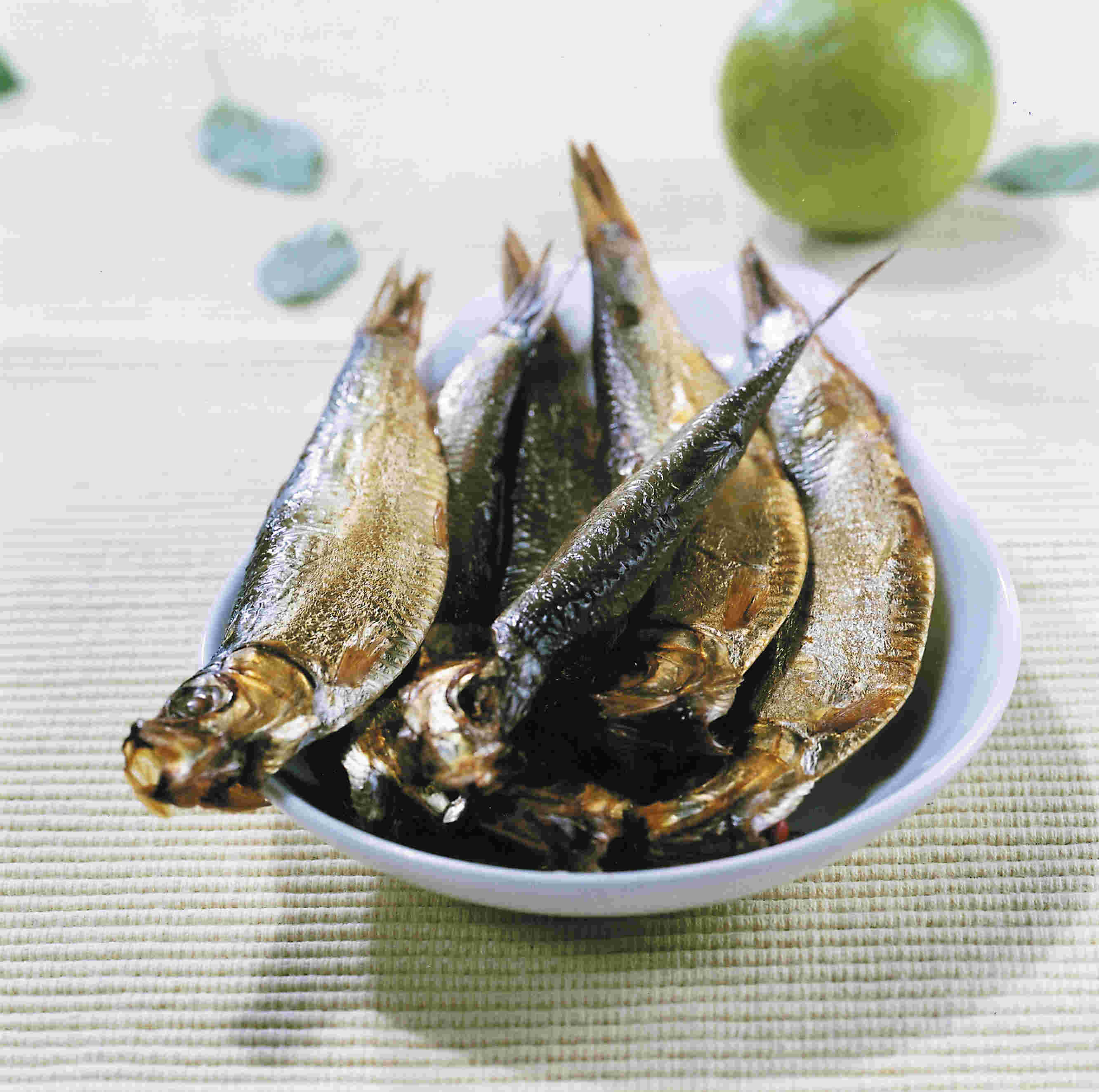 Nahaufnahme von mehreren geräucherten Fischen, die auf einem weißen Teller angerichtet sind, im Hintergrund eine Limette