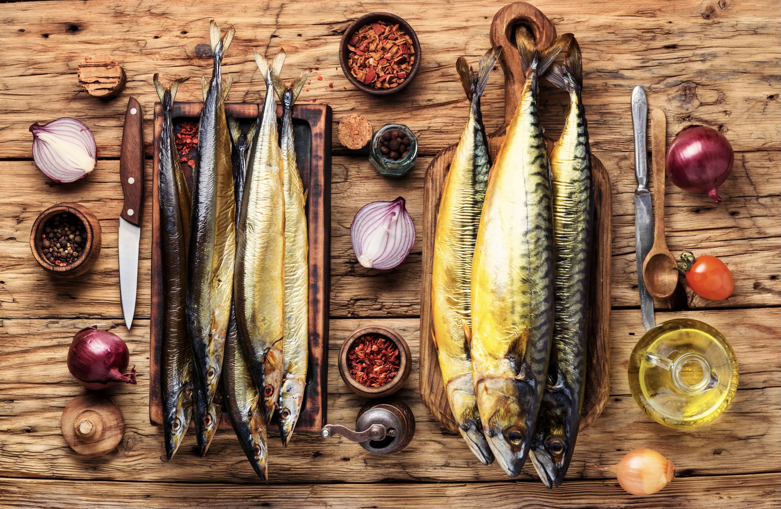 Frische Makrele und Geräucherte Fische mit Gewürzen auf Holzbrett Frische Makrele und geräucherte Fische zusammen mit Zwiebeln, Pfeffer und Öl auf einem rustikalen Holzbrett arrangiert.