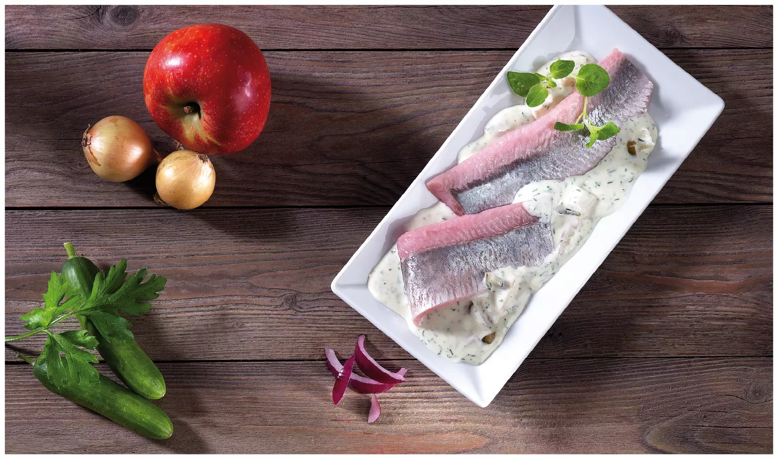 Matjesfilet auf Sahnesauce mit Kräutern auf weißem Teller