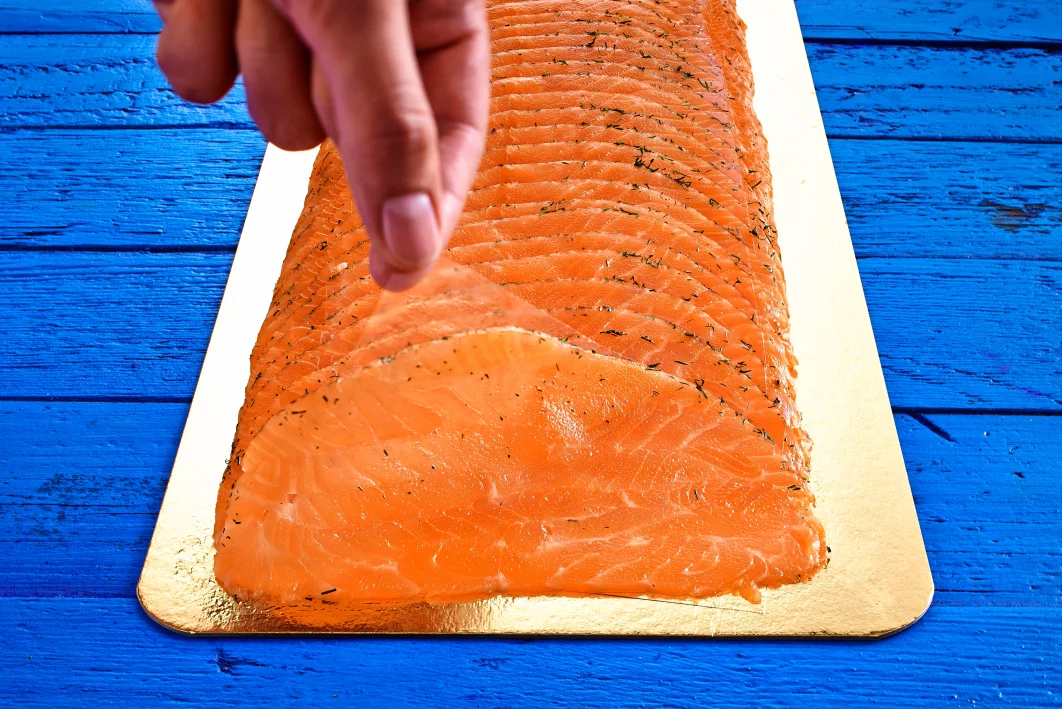 Scheiben Graved Lachs auf goldener Platte, Hand hebt Stück a