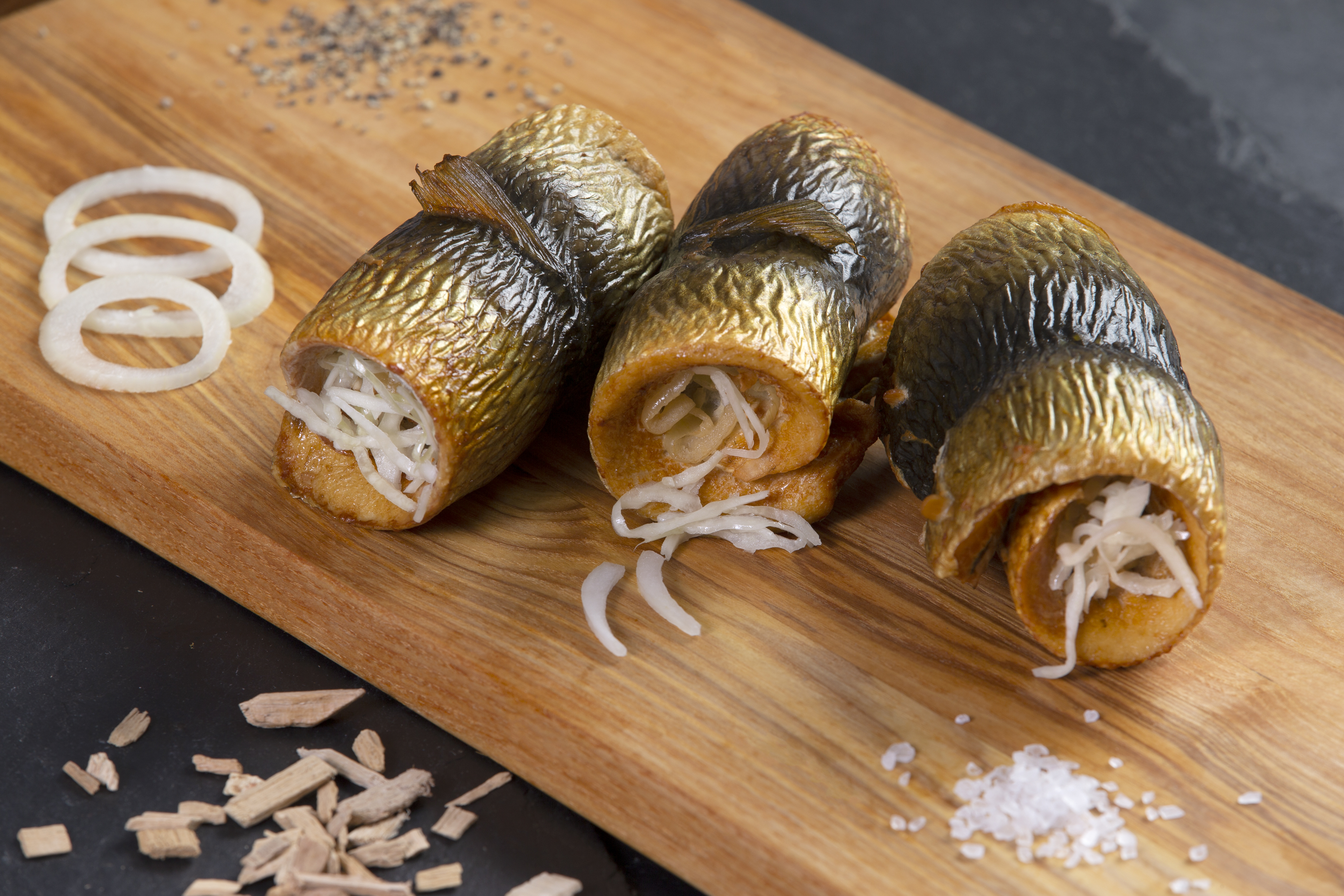 Heringsröllchen auf Holzbrett mit Zwiebelringen Drei Heringsröllchen gefüllt mit Zwiebeln auf einem Holzbrett präsentiert