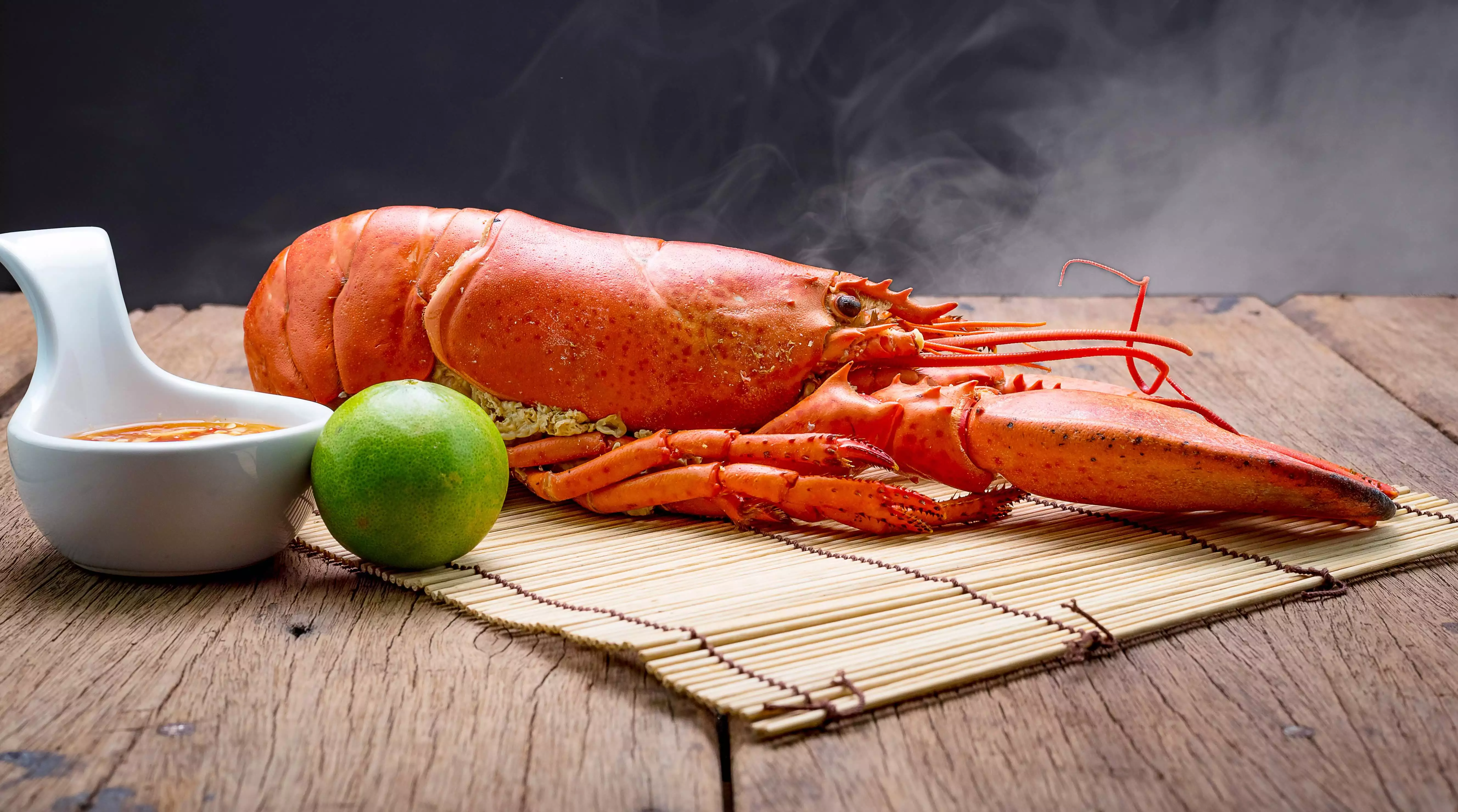 ganzer Hummer, Limette und Dip auf Holzbrett angerichtet