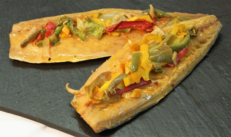 Zwei gebackene Fischfilets, garniert mit roter, grüner und gelber Paprika auf einer dunklen Schieferplatte serviert.