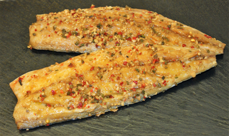 Zwei marinierte Fischfilets mit Kräutern und Gewürzen garniert auf einer dunklen Schieferplatte serviert