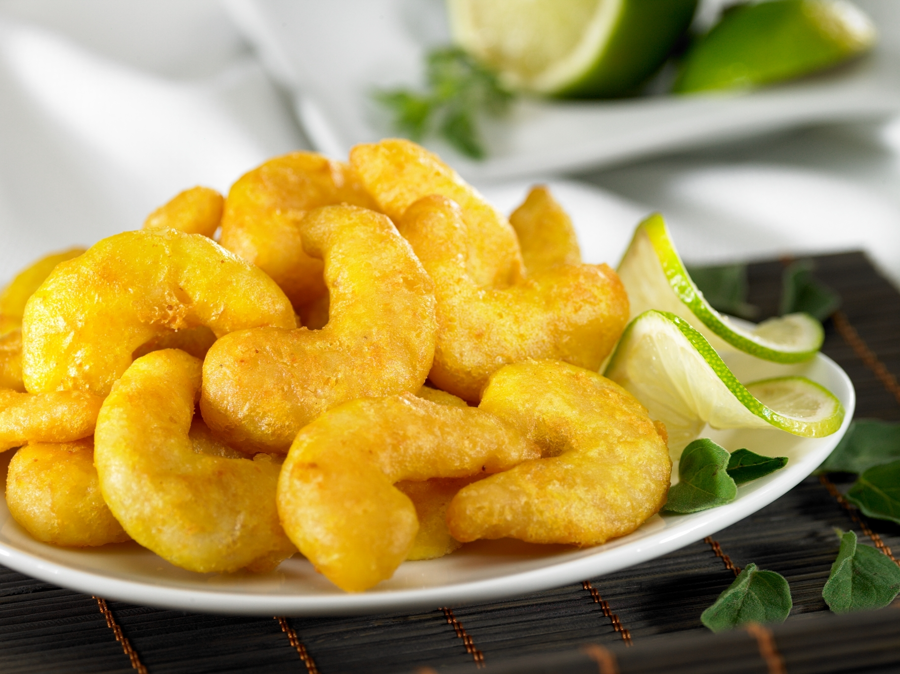 Ein Teller mit knusprig frittierten Garnelen, serviert mit frischen Limettenscheiben auf einem dunklen Platzdeckchen.