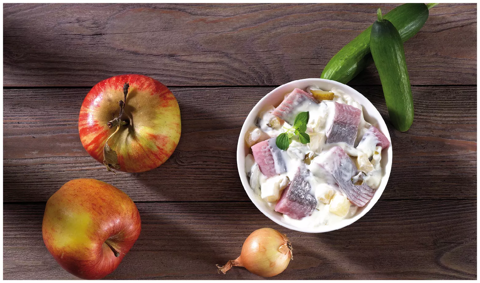 Heringssalat in Schüssel, Apfel, Gurke, Zwiebel daneben