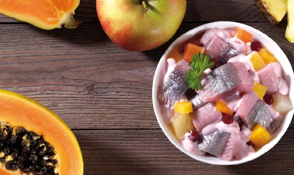 Schüssel Heringssalat mit Obststücken und Joghurt auf Holz